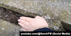 Журналістка видання Kerch.FM демонструє ширину тріщин між плитами Північно-Кримського каналу в районі Керчі, лютий 2023 року